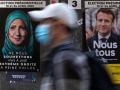 Un peatón pasa delante de un cartel electoral de Macron y otro, vandalizado por un artista callejero, de Le Pen