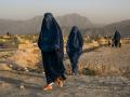 Mujeres afganas con burkas tradicionales pasan frente a un cementerio en Kabul