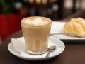 Flat white coffee in transparent glass cup with white foam, behind lightning cake, food on table in cafe.White coffee in a flat transparent glass with foam behind éclairs cake coffee white flat cup drink cafe food symbol black espresso table Set, breakfast, drink, caffeine, cappuccino, morning, restaurant, modern, brown, latte, wooden, office, home, paper, aroma, fresh, broken, plate, nobody, liquid, dessert, round shape, round, delicious, foam