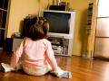 Rear view of little girl sitting on the floor and watching TV in living-room