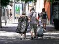 Una pareja de ancianos camina por la calle con un carro de compra.
