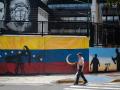 Un hombre pasa junto a un mural pintado en la pared frente a la sede de PDVSA, Venezuela