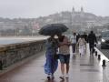 Dos personas se protegen de la lluvia con un paraguas en la playa de Ondarreta, San Sebastián