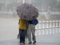 Dos personas comparten paraguas bajo la lluvia en la Playa de San Lorenzo de Gijón