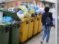 Una mujer camina al lado de contenedores de basura desbordados en Villalba, Lugo