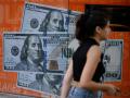 Una mujer pasa junto a una imagen de billetes de cien dólares estadounidenses en Buenos Aires