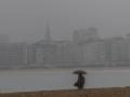 Una mujer se protege de la lluvia con paraguas en la playa de Ondarreta de San Sebastián