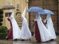 Unos nazarenos de la Hermandad de La Sentencia se protegen de la lluvia con paraguas