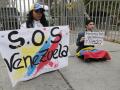 Una pareja de ciudadanos venezolanos sostiene carteles afuera de la embajada de Venezuela este martes, en el barrio de Providencia en Santiago (Chile)