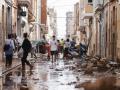 Unas personas caminan por una calle cubierta de lodo en Valencia mientras otras se afanan en las labores de limpieza