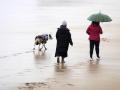 Dos personas pasean con sus perros bajo la intensa lluvia cerca de la orilla de la playa de San Lorenzo, en Gijón