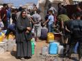 Palestinos intentan recoger agua en un campamento para desplazados en la ciudad de Gaza
