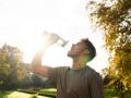 Un joven atleta se hidrata con agua fresca de una botella después de hacer ejercicio en un parque al atardecer durante el verano