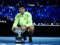 Carlos Alcaraz posa en el suelo de la Rod Laver con el trofeo de campeón del Open de Australia