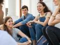 Group of happy young friends sitting in college campus and talking. Cheerful group of  smiling girls and guys feeling relaxed after university exam. Excited millenials laughing and having fun outdoor.