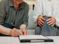 Lawyer, hands of old woman and sign paperwork in home for life insurance, title deed or agreement. Retirement, professional or senior client with signature for policy consent or legal form compliance