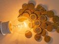 Lit light bulb with coins beside it. Increase in energy tariffs. Efficiency and energy saving.