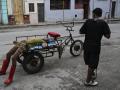 Un hombre descansa sobre un triciclo de carga mientras otra persona pasa caminando en La Habana
