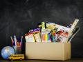 "Suffolk, Virginia, USA - August 22, 2013: A horizontal studio shot of a a donation box for school supplies shot against an authentic school chalkboard. Next to the box is a miniature school bus, world globe and a collection of new pens and pencils."