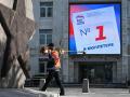 Un hombre con una cortadora de césped pasa junto a una pantalla digital en el edificio de la sede del partido Rusia Unida, que llama a la gente a votar por los candidatos del partido en las próximas elecciones para la cámara baja del parlamento ruso, la Duma Estatal, en Moscú,