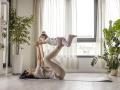 Young fit long hair mother exercise with her two year old child at home near the window