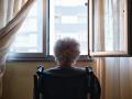 Una mujer mayor en silla de ruedas mira por la ventana de su casa