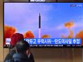 La gente mira una pantalla de televisión que muestra una transmisión de noticias con imágenes de archivo de una prueba de misiles de Corea del Norte