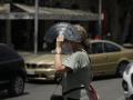 A woman crosses a street and covers herself with a fan in Palma de Mallorca during a heat wave.