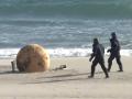 Dos agentes de Policía se aproximan a la enorme bola aparecida en una playa de Japón la semana pasada