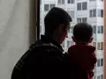 Un padre mirando por la ventana con su hijo en brazos
