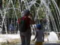 Niños y adultos se refrescan a la sombra, junto a las fuentes públicas del parque del Retiro