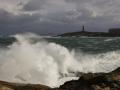 La Coruña sigue en alerta roja por la fuerza del viento y las olas. En la imagen una ola y al fondo la Torre de Hércules