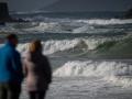 Dos personas observan el mar con olas por el temporal, en la playa de A Lanzada