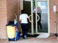 Una trabajadora de la limpieza entra en un edificio con el carrito de la limpieza