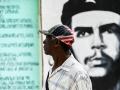 Un hombre con una gorra de EE.UU. camina junto a un letrero con la imagen del Che en La Habana