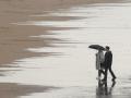 Gente paseando bajo la lluvia en la Playa de San Lorenzo de Gijon