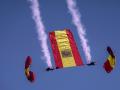 Dos paracaidistas de la Patrulla Acrobática de Paracaidismo del Ejército del Aire portan una bandera de España durante el desfile aéreo en la bahía de San Lorenzo de Gijón