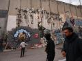 Un niño juega mientras unos hombres pasan junto a un grafiti que representa la reconstrucción de Gaza, en una sección de la barrera de separación de Israel, en Belén, en la Cisjordania