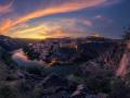 Sunset over the historic city of Toledo seen from Mirador del Valle. Dramatic clouds, river reflection, and golden evening light illuminate the skyline.