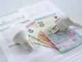 Un enchufe, una bombilla y billetes en euros en una factura de electricidad.