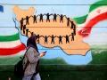 Una mujer pasa junto a la bandera y el mapa de Irán pintados en una pared en Teherán