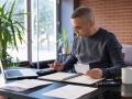 Mid aged man reviewing paper financial statements at home