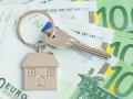 Llaves de casa y una pequeña casa sobre billetes de fondo