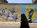 Mujeres iraníes pasan junto a un mural antiestadounidense y antiisraelí en Teherán