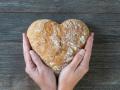 Unas manos sosteniendo un pan con forma de corazón, alimento esencial en toda dieta