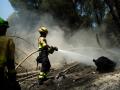 Bomberos rocían agua sobre el terreno para evitar que el fuego se reavive tras lograrse controlar un incendio cerca de La Adrada