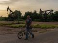 Un hombre empuja una bicicleta frente a pozos petroleros abandonados en Maracaibo, estado Zulia, Venezuela