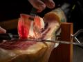 Close up of cutter gourmet hands slicing acorn fed iberian ham. Typical and traditional spanish delicatessen pork food.