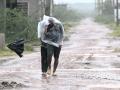 Unos hombres utilizan una lámina de plástico para cubrirse durante la lluvia en Kakinada