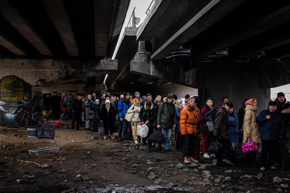 Evacuees stand under a destroyed bridge as they flee the city of Irpin, northwest of Kyiv, on March 7, 2022. - Ukraine dismissed Moscow's offer to set up humanitarian corridors from several bombarded cities on Monday after it emerged some routes would lead refugees into Russia or Belarus. The Russian proposal of safe passage from Kharkiv, Kyiv, Mariupol and Sumy had come after terrified Ukrainian civilians came under fire in previous ceasefire attempts. (Photo by Dimitar DILKOFF / AFP)
